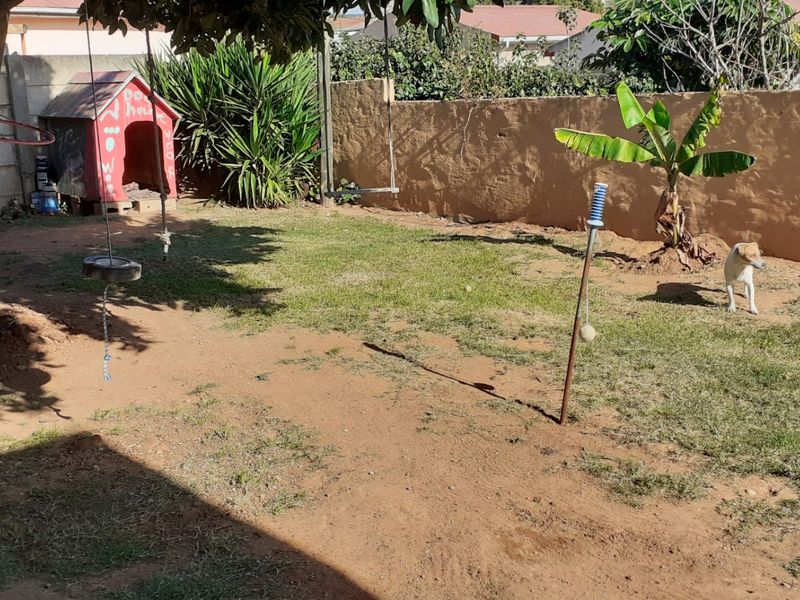 A private rear garden featuring a boundary wall, mature tree, and lawn area with potential for landscaping improvements.