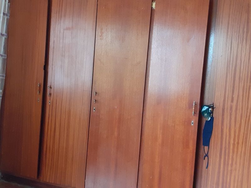 A bedroom featuring a large, dated built-in wooden wardrobe with multiple doors.