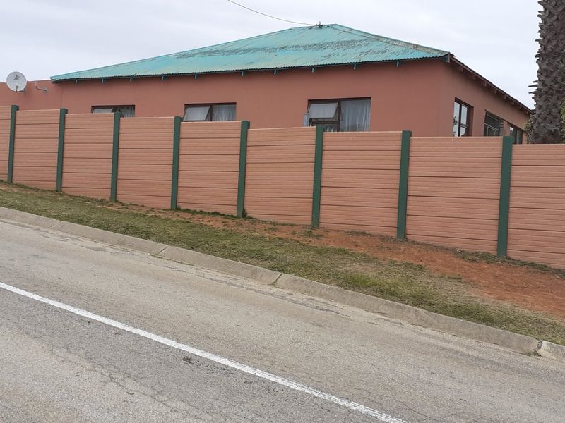 Street view of a residential property featuring a long precast concrete boundary wall and a corrugated metal roof.