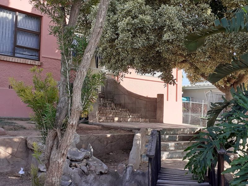 Rear exterior view of the property featuring a brick staircase, retaining walls, and established garden landscaping.
