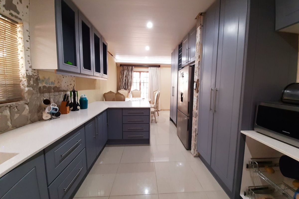 A galley-style kitchen featuring modern grey cabinetry and white countertops, currently requiring completion of wall finishes and backsplash installation.