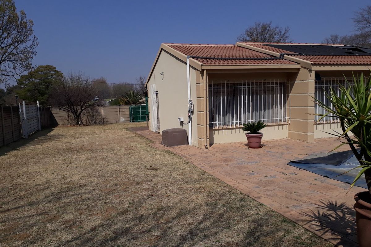 Rear view of the property featuring a paved patio area, tiled roof, and a spacious backyard with perimeter walling.