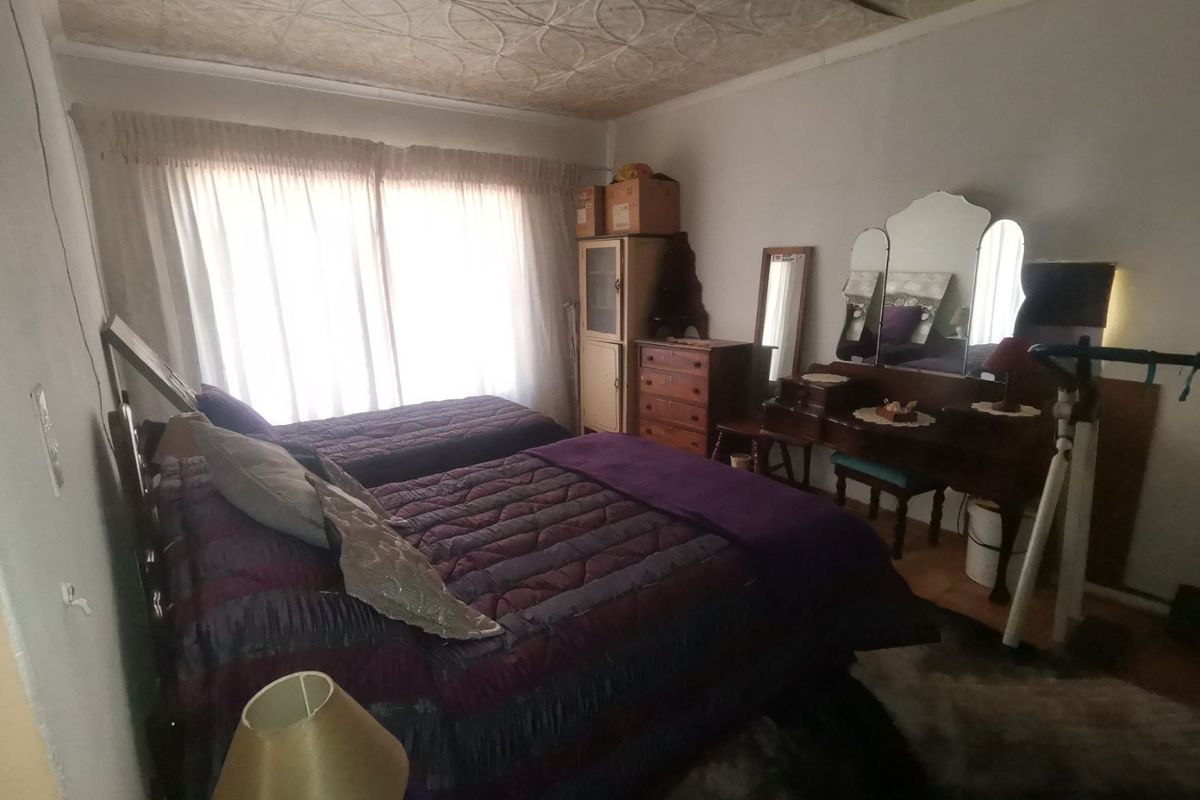 A bedroom featuring a decorative patterned ceiling and large window with curtains, providing natural light to the space.