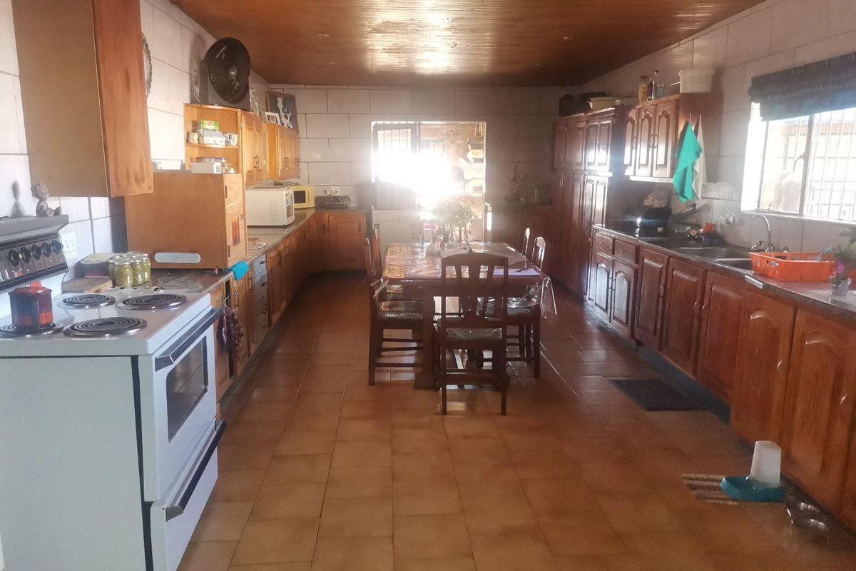 Spacious farmhouse kitchen featuring extensive wooden cabinetry, tiled flooring, a timber-clad ceiling, and a large central dining area with direct outdoor access.