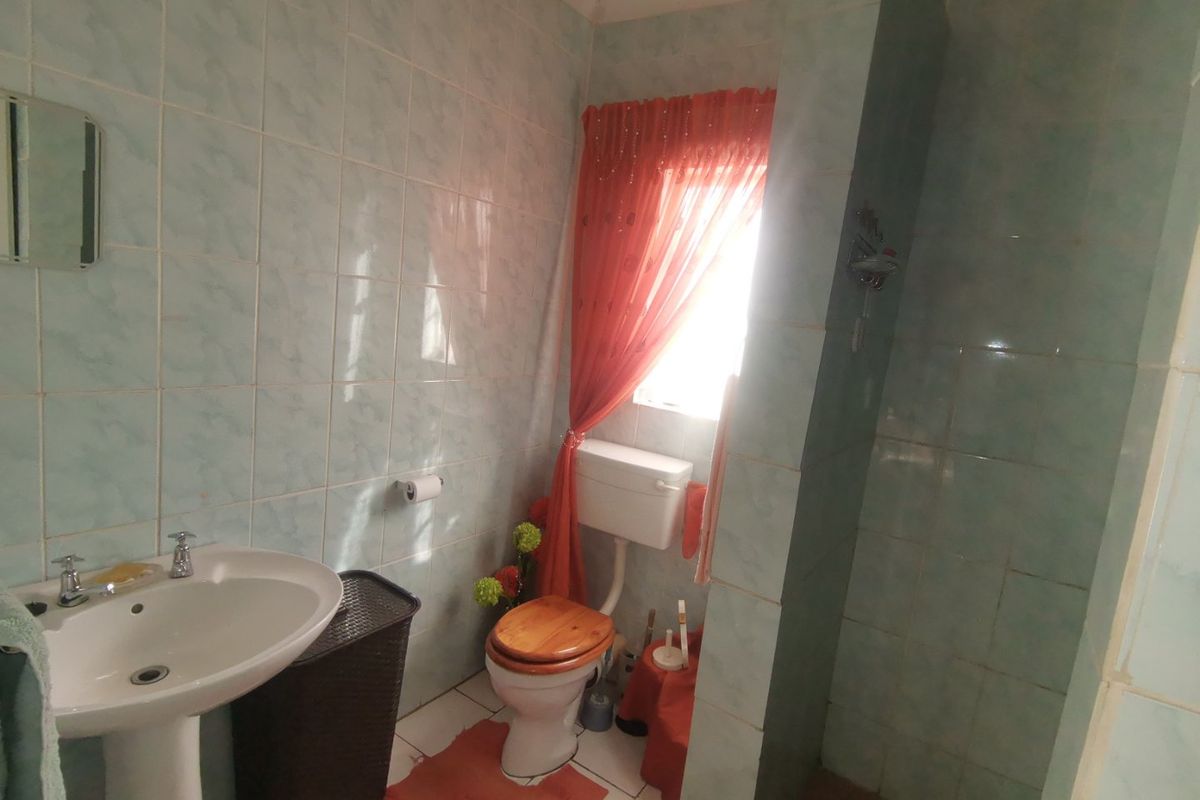 A functional bathroom featuring a pedestal basin, a toilet, and a tiled shower enclosure with light blue wall tiling.