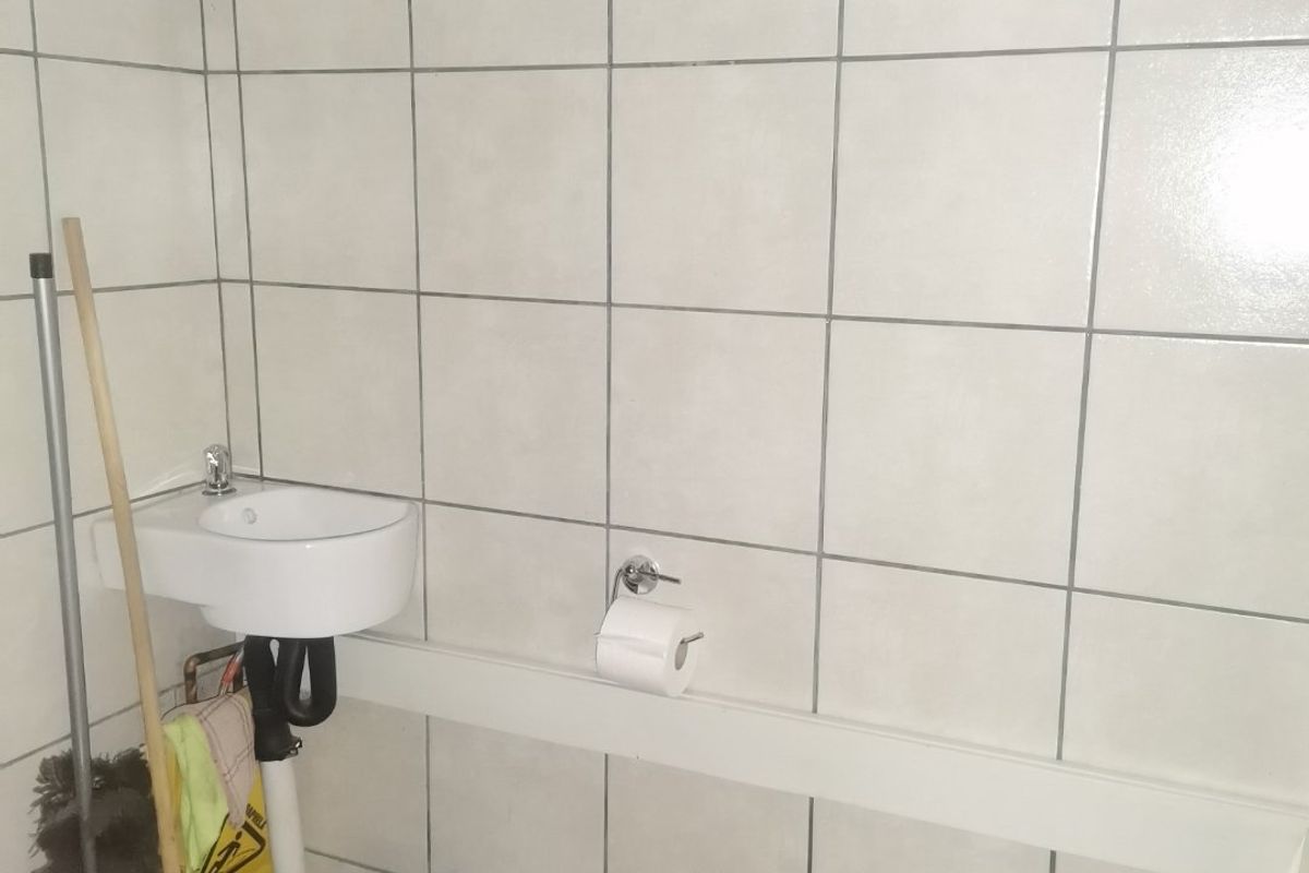 A compact bathroom featuring a wall-mounted basin, toilet, and an exposed electric water heater unit with visible plumbing connections.