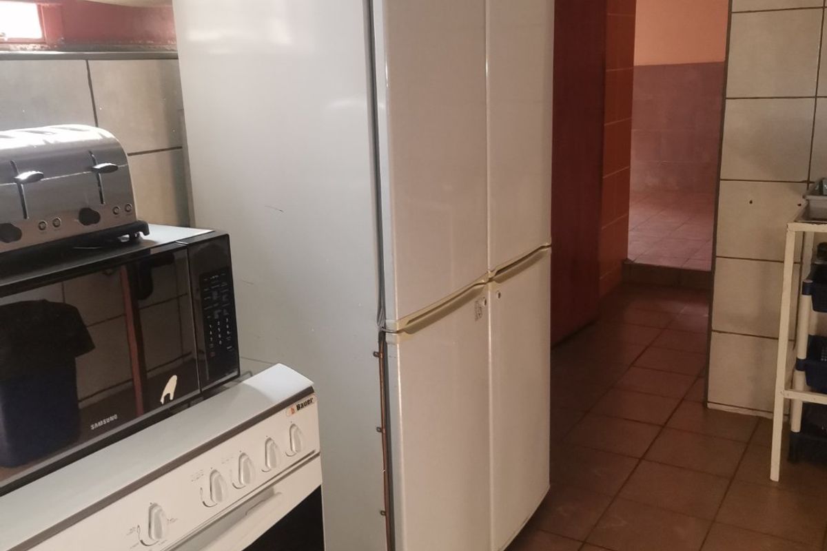 A functional kitchen area featuring tiled flooring, wall-mounted extractor fan, and built-in stove, providing access to an adjacent room.