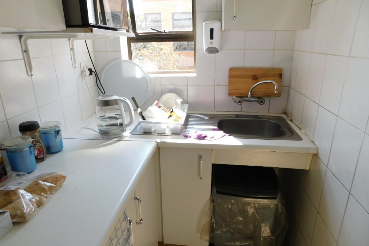 A compact kitchenette featuring a stainless steel sink, tiled splashbacks, and basic cabinetry, suitable for a small office or utility space.
