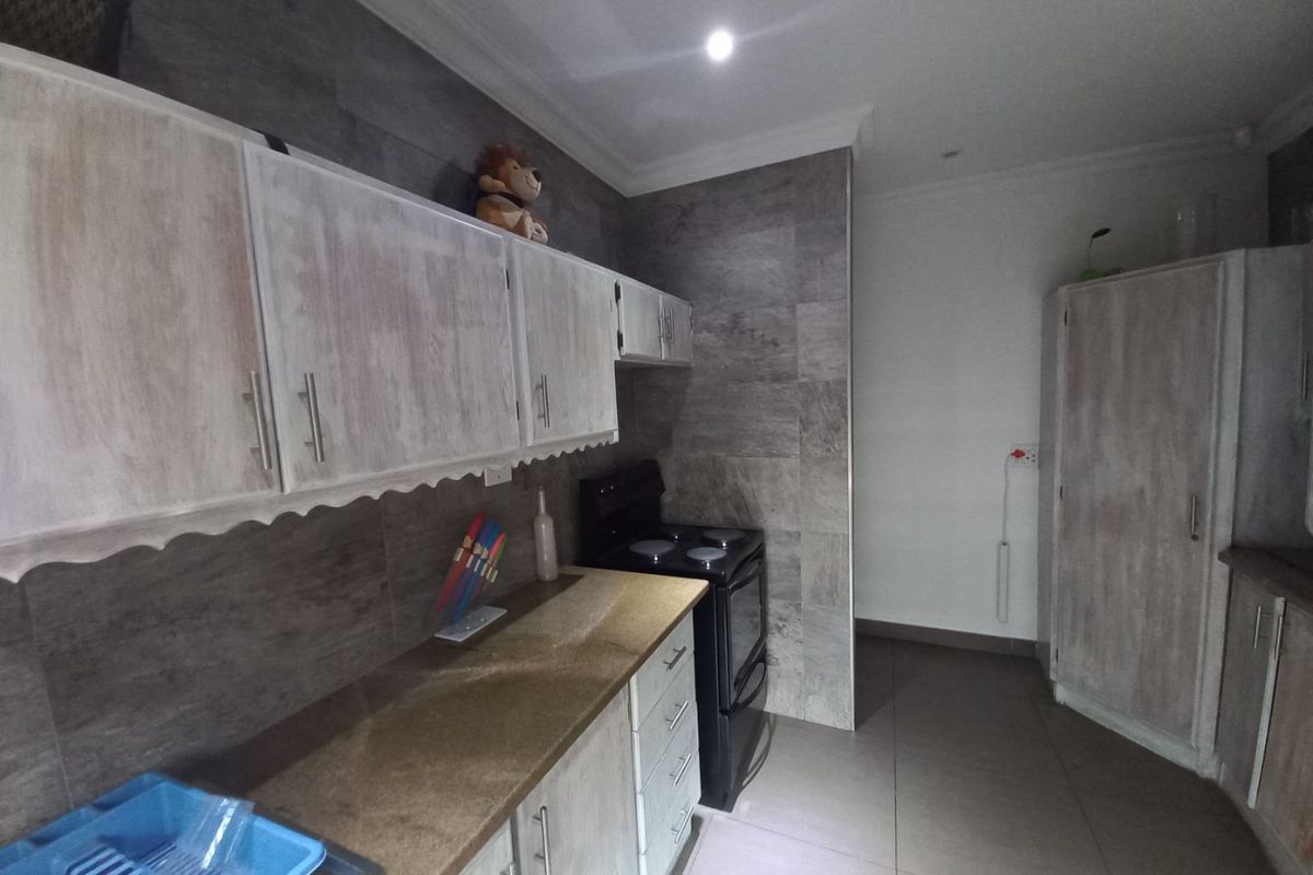 A functional kitchen featuring built-in cabinetry, stone-look countertops, tiled splashbacks, and a freestanding stove.