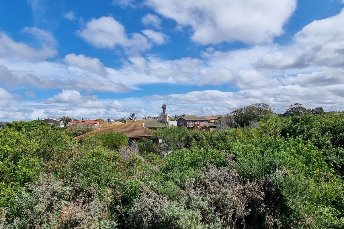 A scenic view overlooking a residential neighborhood surrounded by dense, established native vegetation under a bright, cloudy sky.
