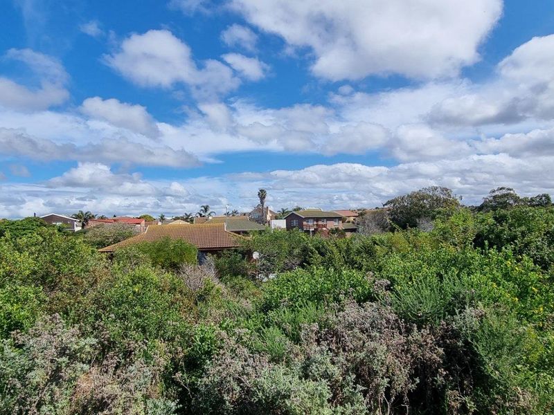 A scenic view overlooking a residential neighborhood surrounded by dense, established native vegetation under a bright, cloudy sky.