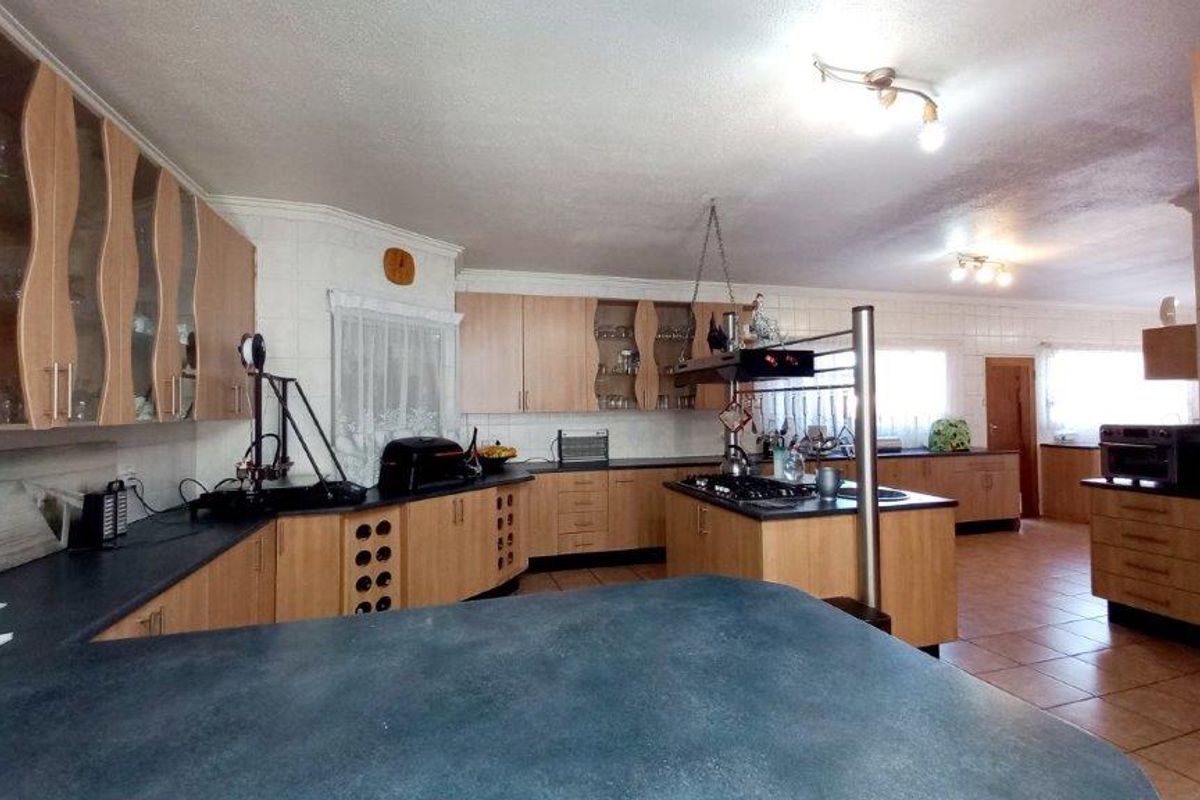 Spacious kitchen featuring extensive laminate cabinetry, dark countertops, a central island with a gas hob, and tiled flooring throughout.