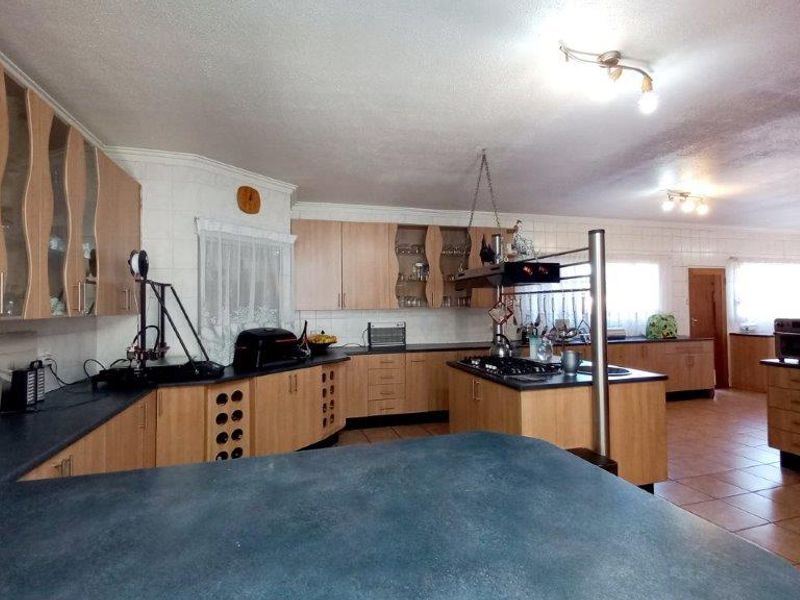 Spacious kitchen featuring extensive laminate cabinetry, dark countertops, a central island with a gas hob, and tiled flooring throughout.