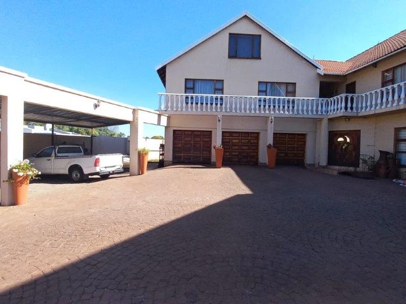 Spacious front exterior featuring a triple garage, extensive paved driveway, covered carport, and an upper-level balcony with classic balustrade detailing.