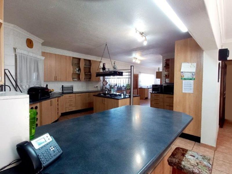 Spacious kitchen featuring extensive laminate cabinetry, a central island with a built-in hob, and tiled flooring, offering a functional layout with ample storage space.