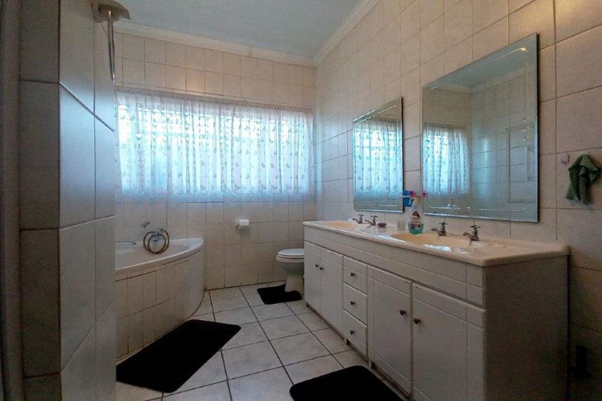 A functional bathroom featuring a double vanity with integrated sinks, a corner bathtub, and wall-to-wall tiling.