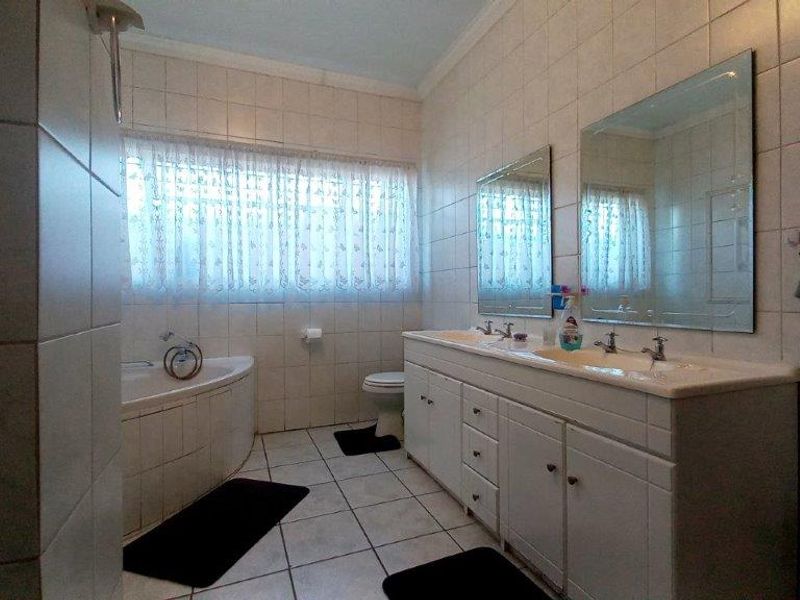 A functional bathroom featuring a double vanity with integrated sinks, a corner bathtub, and wall-to-wall tiling.