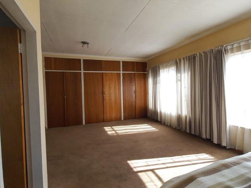 Spacious bedroom featuring extensive built-in wooden cabinetry, neutral carpeting, and large windows that provide ample natural light.