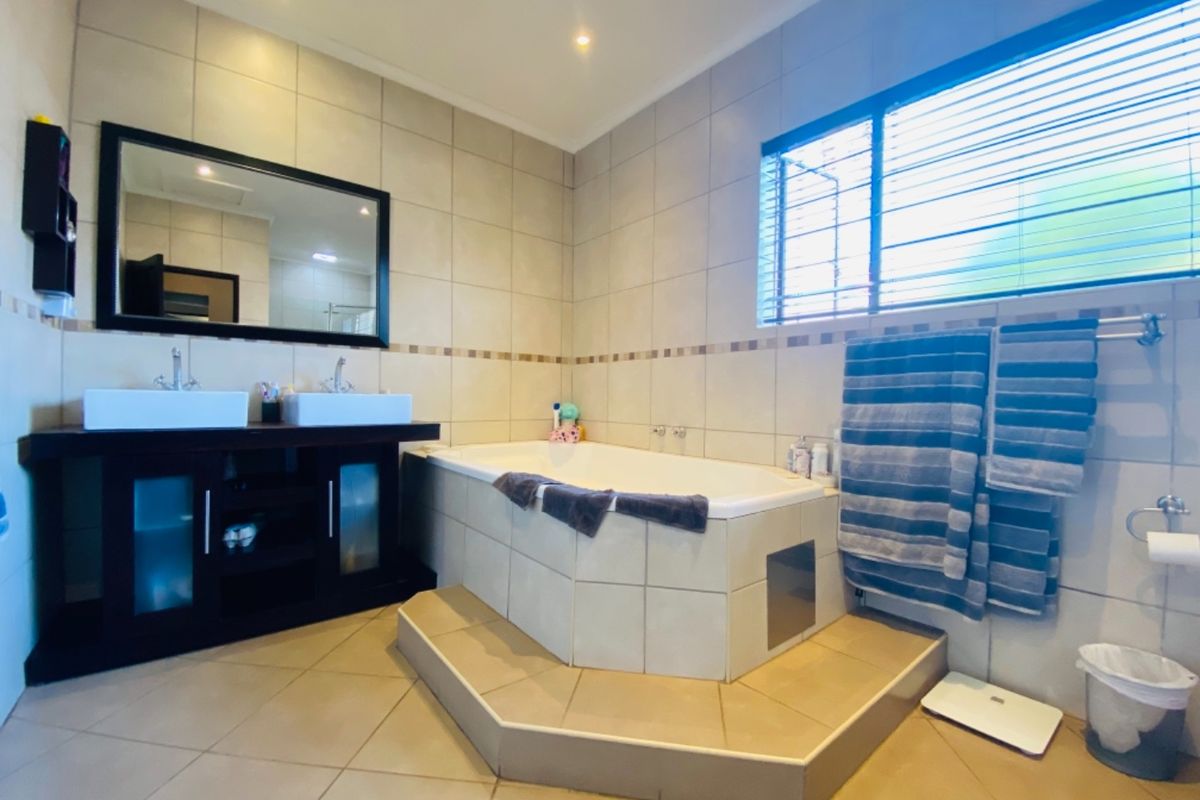 A well-maintained bathroom featuring a built-in bathtub, double vanity with vessel sinks, and neutral wall and floor tiling.