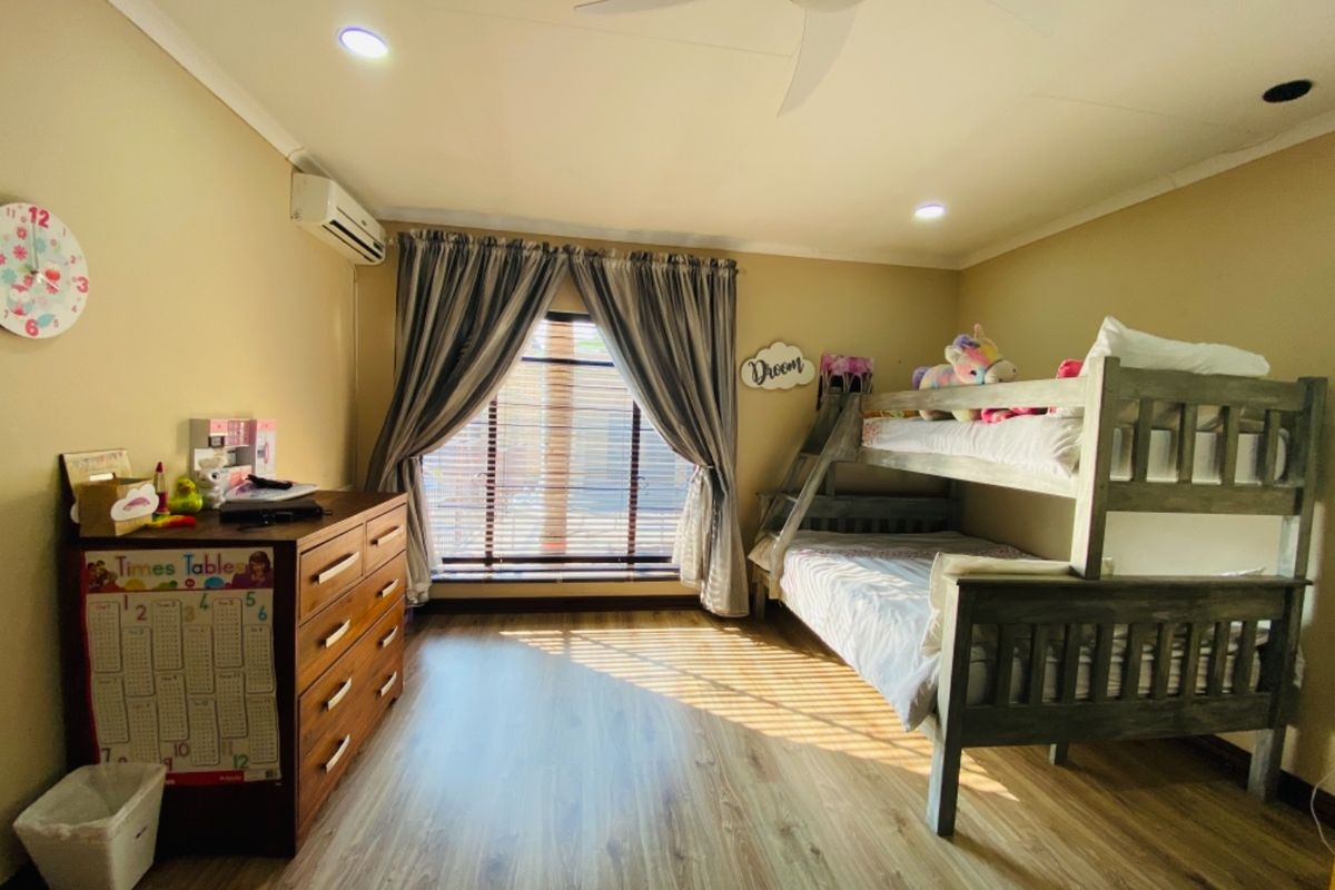 A well-maintained bedroom featuring wood-look laminate flooring, a ceiling fan, and a wall-mounted air conditioning unit.