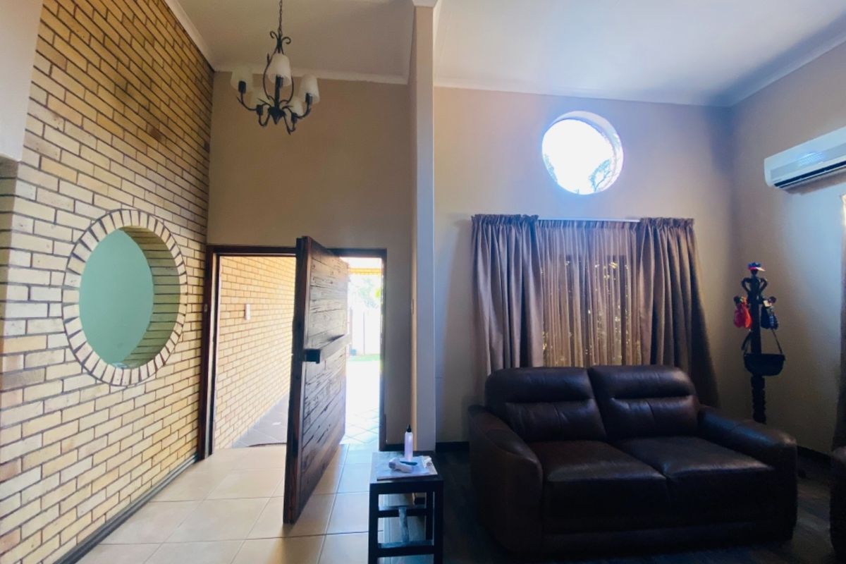 Living room featuring a distinctive circular window, exposed brick feature wall, tiled flooring, and a split-system air conditioning unit.