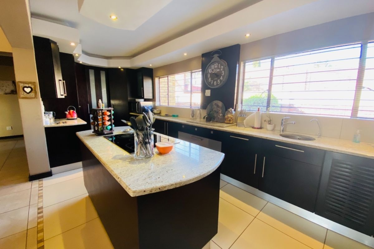 Modern kitchen featuring dark cabinetry, granite countertops, a central island with a built-in hob, and tiled flooring with recessed ceiling lighting.