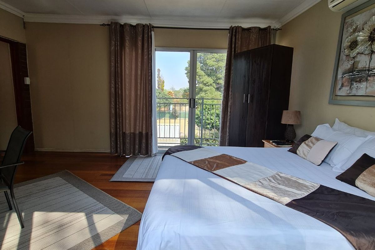 Spacious bedroom featuring polished timber flooring, a wall-mounted air conditioning unit, and sliding glass doors opening onto a private balcony.