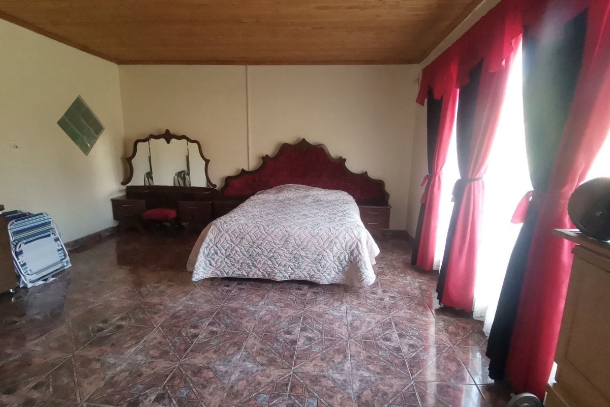 Spacious bedroom featuring tiled flooring, a wooden ceiling, and large windows with curtains, providing a functional and well-lit sleeping area.