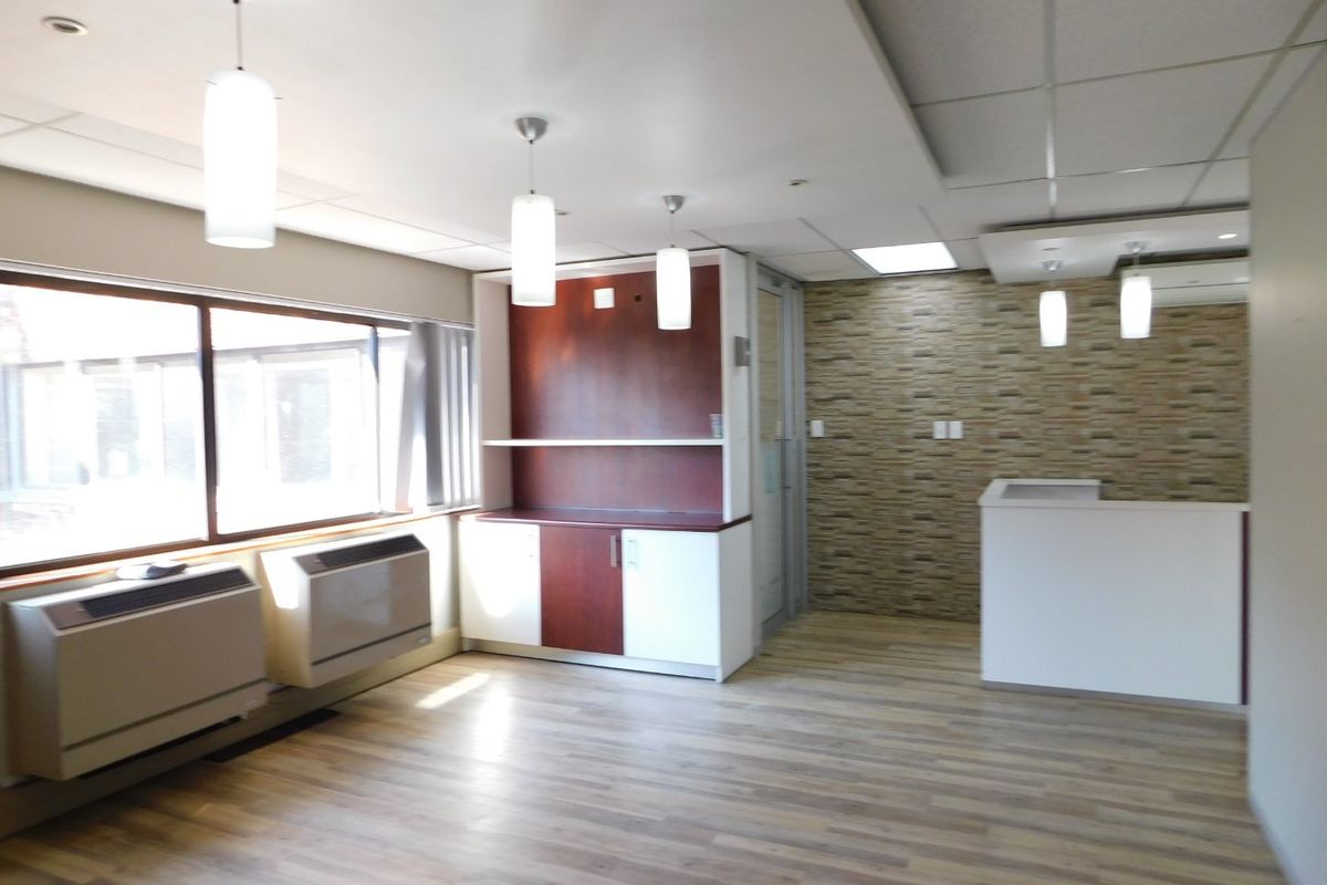 A bright, modern office space featuring wood-look laminate flooring, built-in cabinetry, a stone veneer accent wall, and integrated HVAC units.