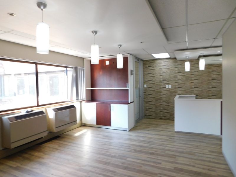 A bright, modern office space featuring wood-look laminate flooring, built-in cabinetry, a stone veneer accent wall, and integrated HVAC units.