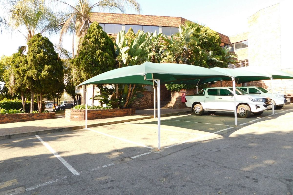 Exterior view of the office building featuring paved parking bays with shade cloth carports and established garden landscaping.