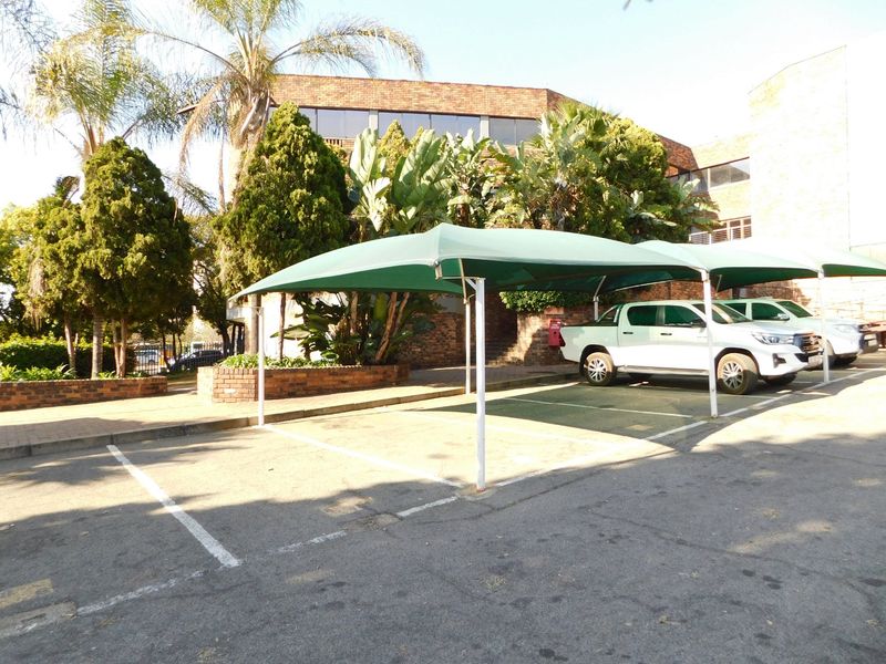 Exterior view of the office building featuring paved parking bays with shade cloth carports and established garden landscaping.