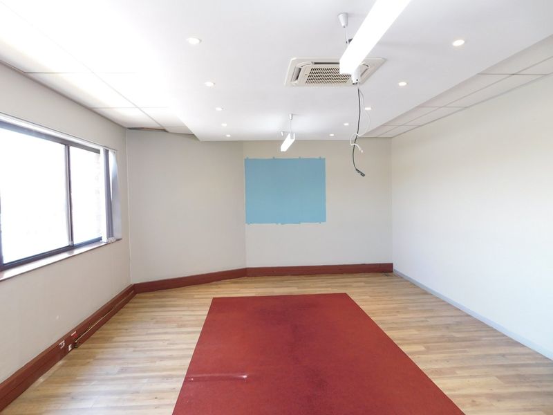 An empty office space featuring laminate flooring, recessed ceiling lighting, and a built-in cassette air conditioning unit.