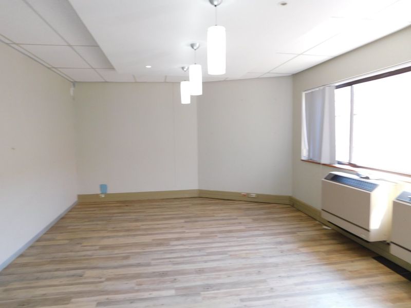 A vacant office space featuring wood-look flooring, a suspended ceiling with pendant lighting, and a built-in HVAC unit.