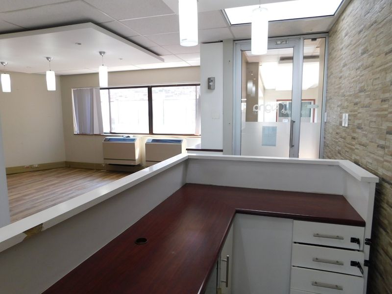 A professional office space featuring a built-in reception desk, stone accent wall, glass entry door, and wood-look flooring with integrated HVAC units.