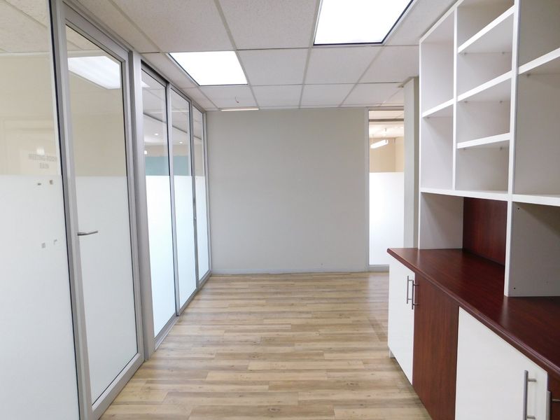 A clean, modern office space featuring glass partitions, built-in storage cabinetry, recessed ceiling lights, and durable laminate flooring.