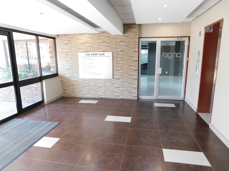 Modern office building entrance lobby featuring tiled flooring, a stone-clad feature wall, and glass entry doors with elevator access.