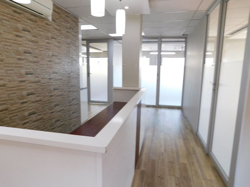 Modern office space featuring a built-in reception desk, glass partitions, stone-cladding feature wall, and wood-look laminate flooring.