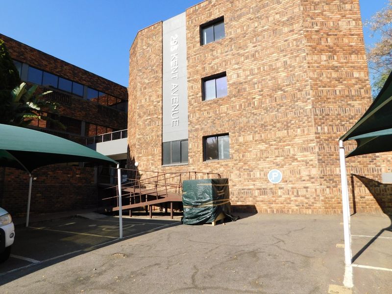 Front exterior view of the office building at 298 Kent Avenue, featuring brick facade, parking area with shade cloth carports, and a wheelchair access ramp.