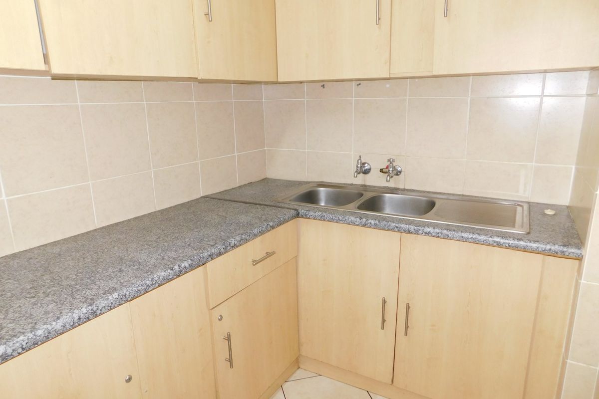 A functional kitchenette featuring light wood-finish cabinetry, granite-look laminate countertops, and a stainless steel double sink with tiled splashbacks.