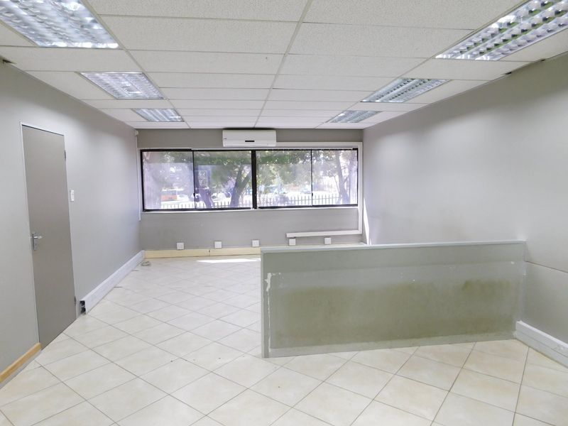 An empty office space featuring tiled flooring, a suspended ceiling with recessed lighting, a split-system air conditioner, and a central partition wall.