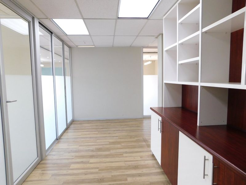 A bright, vacant office space featuring modern laminate flooring, built-in storage cabinetry, and glass partition walls, ideal for a professional workspace.
