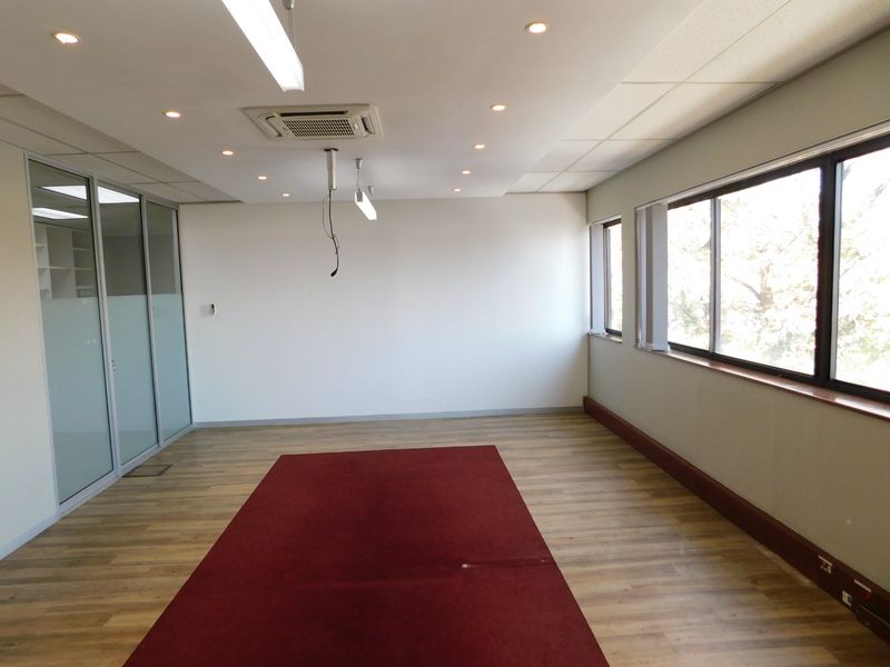 A vacant office space featuring laminate flooring, recessed ceiling lighting, a cassette air conditioning unit, and glass partition walls.