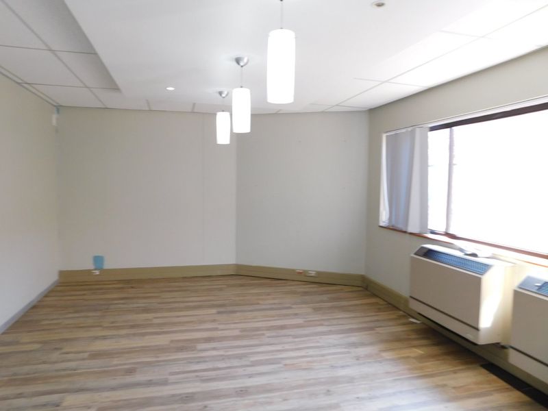 A vacant office space featuring wood-look flooring, suspended ceiling tiles, pendant lighting, and a built-in PTAC air conditioning unit.