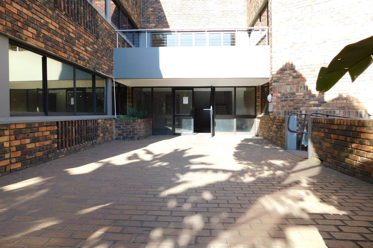 A paved rear courtyard area featuring a brick facade, large windows, and a metal balcony railing above the main entrance.