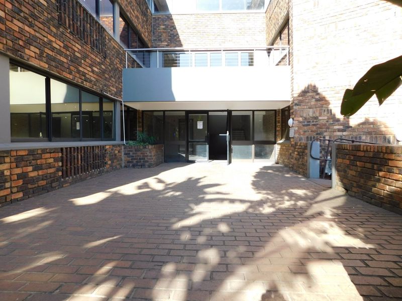 A paved rear courtyard area featuring a brick facade, large windows, and a metal balcony railing above the main entrance.