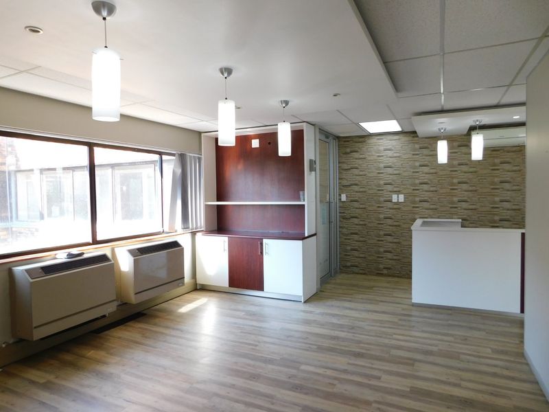A bright, modern office space featuring a reception desk, built-in cabinetry, stone veneer accent wall, and wood-look laminate flooring.