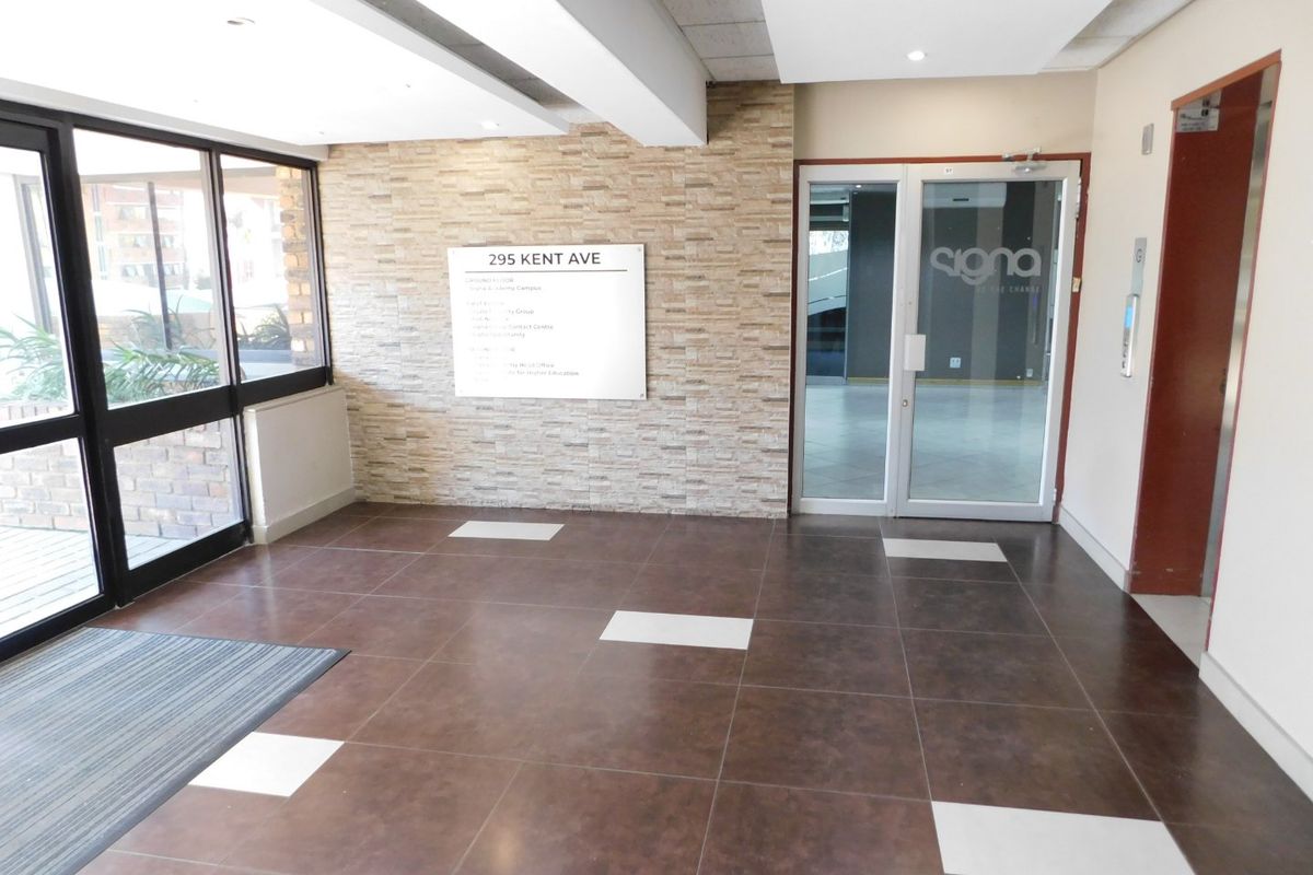 A clean and professional office building entrance lobby featuring tiled flooring, a stone-clad feature wall, and glass entry doors with elevator access.