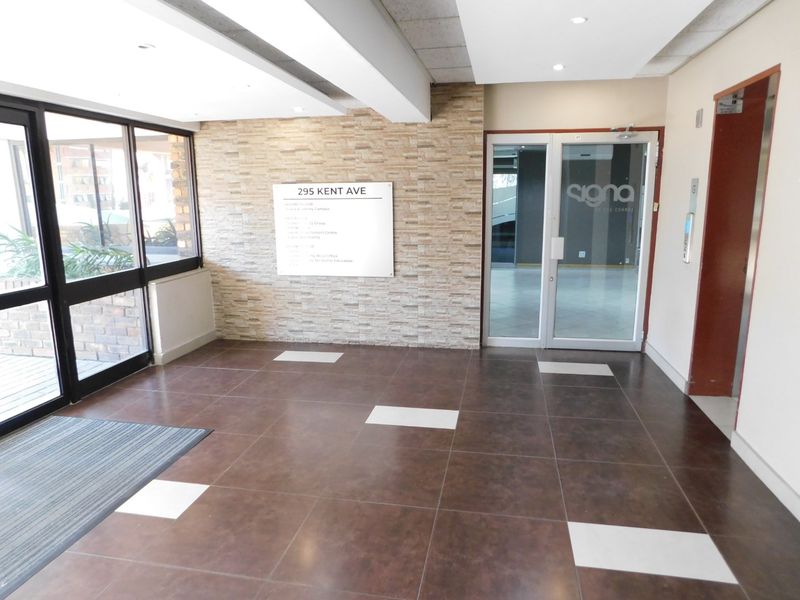 A clean and professional office building entrance lobby featuring tiled flooring, a stone-clad feature wall, and glass entry doors with elevator access.