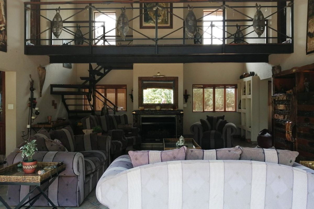 Spacious double-volume living area featuring a mezzanine level, exposed steel staircase, and a central fireplace with a stone surround.
